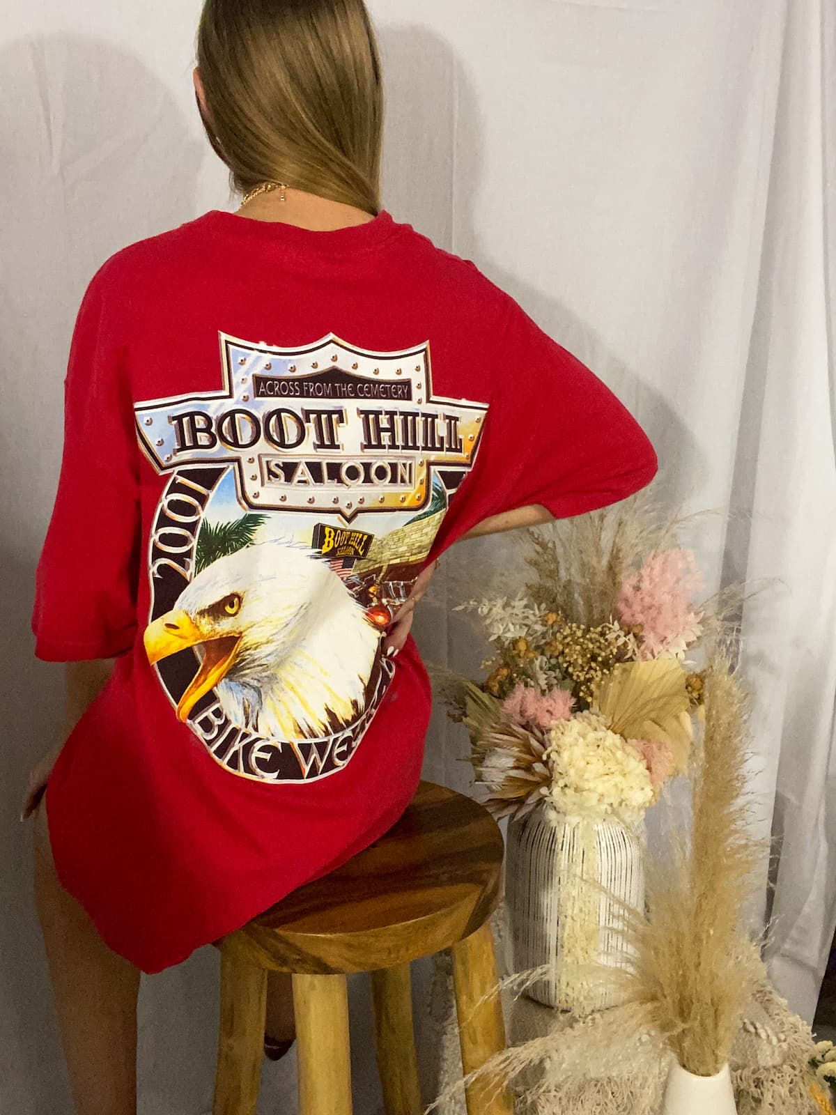 Person wearing a red Harley Davidson t-shirt with an eagle graphic and text, sitting on a stool.